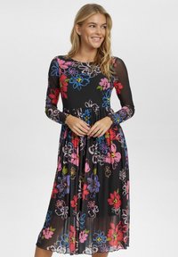 Blommig klänning med långa ärmar, svart bakgrund och färgglada blommönster i rosa, blått och grönt; åtsittande midja med en flödande kjol.
