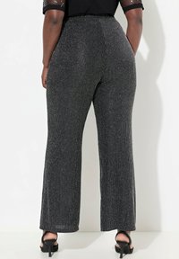 Zwart en zilver gestreepte wijde broek met hoge taille, van een textuurstof met een subtiele glans. Gekozen in combinatie met zwarte hakken.