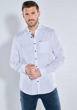 Weißes Langarmhemd aus leichtem Stoff. Es hat einen Knopfverschluss vorne, eine Brusttasche und dunkle Knöpfe, die einen Kontrast zur hellen Farbe bieten.