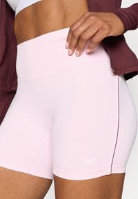 Světle růžové sportovní šortky vyrobené z pružného materiálu s vysokým pasem a jemnými švy. Obsahují malé bílé logo Nike.
