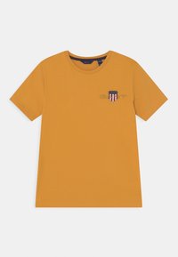 Musztardowa żółta koszulka z krótkim rękawem wykonana z bawełny, z małym haftowanym logo w kształcie tarczy na lewej piersi.