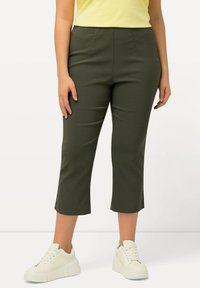 Pantalons cropped vert olive au design ajusté, avec une taille haute et des plis subtils, associés à des baskets blanches à plateforme.