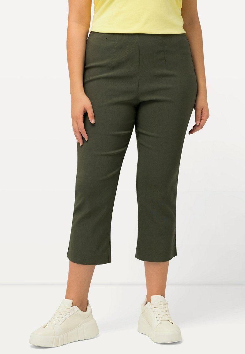 Pantalons cropped vert olive au design ajusté, avec une taille haute et des plis subtils, associés à des baskets blanches à plateforme.