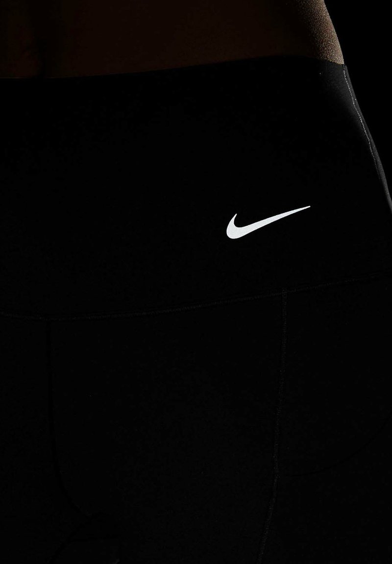 Schwarze Sportleggings aus dehnbarem Material mit einem weißen Nike-Logo. Sie haben eine glatte Textur und ein enges Design.