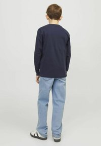 Camisa de manga larga azul marino con cuello redondo, combinada con jeans de color azul claro y zapatillas en blanco y negro, vista desde atrás.
