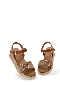 Sandalias de cuero marrón con tiras de paja trenzadas, suela plana con cuña y hebillas doradas. Cuenta con correas ajustables en el tobillo para un mejor ajuste.