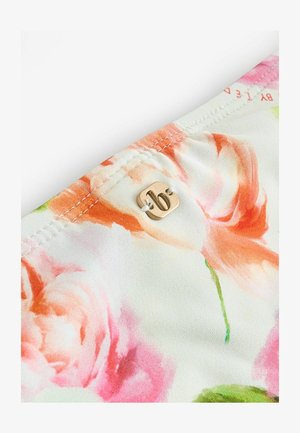 Bloes met bloemenprint in lichtgewicht stof, met zachte perzik- en roze rozen op een crèmekleurige achtergrond. Goudkleurige hardwaredetails zichtbaar.