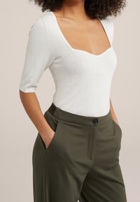 Vit ribbad bodysuit med fyrkantig halsringning och korta ärmar, kombinerad med olivgröna skräddarsydda byxor med sidfickor och en knapp.