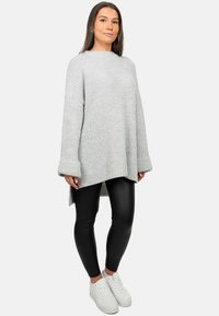 Maglione grigio chiaro oversize a maglia con texture a costine e spalle scese, abbinato a leggings neri e sneakers bianche.