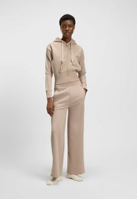 Felpa con zip beige con cordini, orlo a coste, abbinata a pantaloni ampi coordinati. Tessuto liscio, design minimalista, texture sottili.