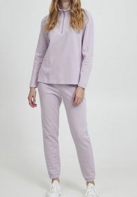 Sudadera morada con cuello de media cremallera y mangas largas, combinada con pantalones joggers ajustados a juego. Tejido suave, ajuste casual y puños elásticos.