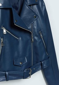 Veste de moto en cuir bleu marine avec des revers diagonaux, plusieurs poches zippées, une ceinture à boucle et des accents en métal argenté.