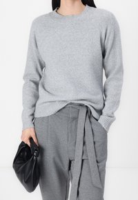 Pull en maille douce gris clair avec un col rond et un ourlet côtelé. Associé à un pantalon gris avec une ceinture nouée et un sac noir.