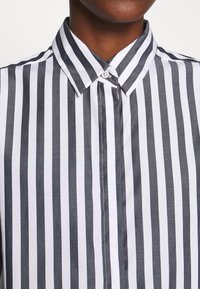 Knäppskjorta med ett grått och vitt vertikalt randigt mönster, med en strukturerad krage och mjuk tygtextur.