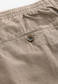 Pantaloni corti in tessuto khaki con vita elasticizzata, chiusura con bottone sulla tasca posteriore e un aspetto testurizzato simile al lino.