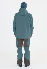 Turkoosi ja harmaa vettä hylkivä takki, jossa on huppu ja siihen sopivat cargo-tyyliset housut, joissa on vahvistetut polvet ja rento istuvuus.