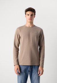 Beige lange mouw T-shirt met een textuur, geribbelde stof. Heeft een ronde halslijn en een klein logo geborduurd op de borst.