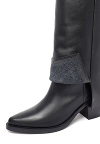 Stivale in pelle nera alta fino al ginocchio con punta affusolata, caratterizzato da un risvolto in camoscio grigio e un tacco spesso. Texture liscia con finitura opaca.