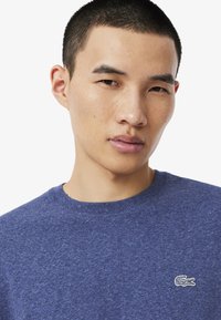 Sininen pyöre äkauluksinen t-paita, joka on valmistettu tekstuurikankaasta. Paidassa on pieni valkoinen brodeerattu logo rinnassa, ja se on minimalistinen lyhythihainen malli.