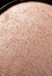 Illuminateur en poudre pressée dans une teinte chaude et métallique de rose doré. Texture lisse avec un léger éclat et des détails de surface inégaux.