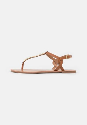 Brune læder flip-flop sandaler med guldfarvede udsmykninger langs stroppen. Har en krydsgående ankelrem og flad sål.