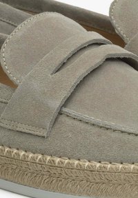 Szare zamszowe loafersy z szerokim paskiem i teksturowaną plecioną podeszwą. Charakteryzują się miękkim wykończeniem i minimalnymi detalami z szycia wzdłuż krawędzi.
