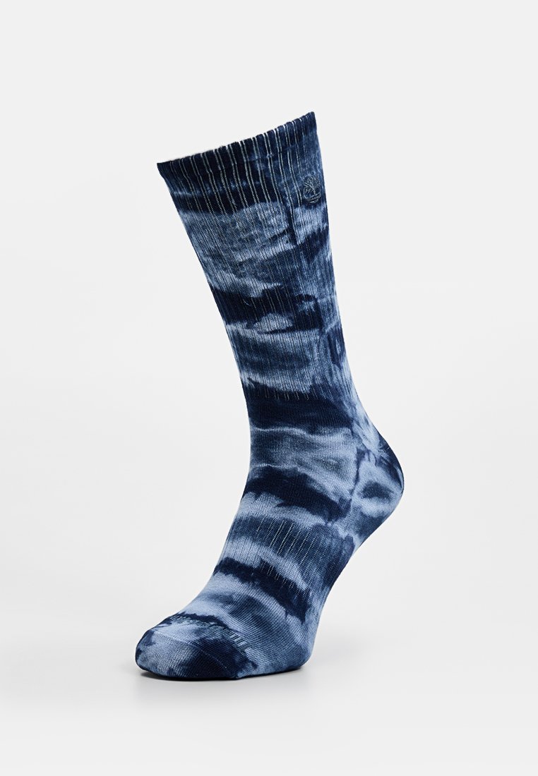 Calzini crew tie-dye blu con parte superiore a coste, un mix di tonalità scure e chiare, e una texture liscia, con un logo discreto vicino al polsino.