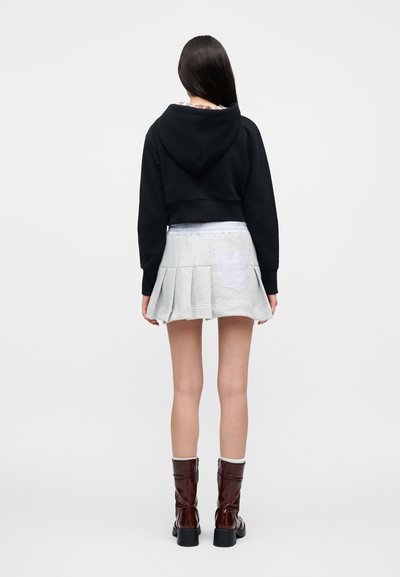 Μαύρο κοντό φούτερ με κουκούλα, γκρι πλισέ φούστα με τσεπάκι καρώ, καφέ λαμπερά μποτάκια αστραγάλου με χοντρά τακούνια και ριμπ κάλτσες.