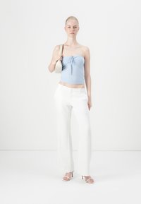 Top sem alças azul claro com um detalhe de laço na frente, combinado com calças de linho brancas de corte solto e sandálias de salto nude. Bolsa simples.