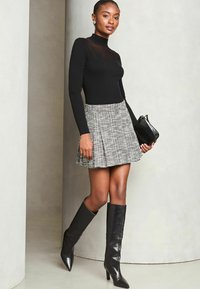 Mustat ribbed turtleneck, harmaa ruudullinen plisseerattu hame, polvipituiset mustat nahka korkokengät, pitämättö mustaa käsilaukkua.