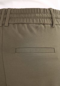 Olijfgroene broek met een elastische tailleband met geplooide textuur en een enkele achterzak voor opslag. Gladde stof met minimale details.