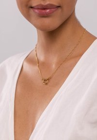 Goldkette mit miteinander verbundenen runden Anhängern, die auf einem Schlüsselbein ruht, kombiniert mit einem tiefen V-Ausschnitt in Weiß, glatte Textur.