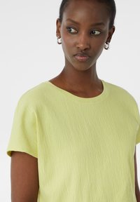 Zielono-limonkowa, teksturowana bluzka z krótkim rękawem, z okrągłym dekoltem, z delikatnymi poziomymi liniami i miękkim, lekkim materiałem.