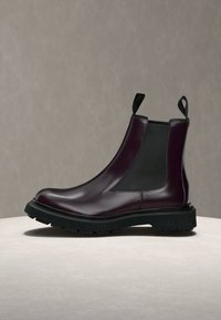 Bottine Chelsea en cuir violet foncé avec panneaux latéraux élastiques noirs et semelle noire épaisse sur une surface claire.