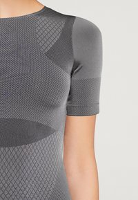 Short-sleeve athletic top in dark gray featuring textured geometric patterns and smooth sections, made from stretchable, breathable material.