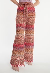 Pantalons larges avec un motif en zigzag présentant des couleurs brunes, rouges et bleues. Texture transparente avec un lien à la taille et un ourlet ondulé.