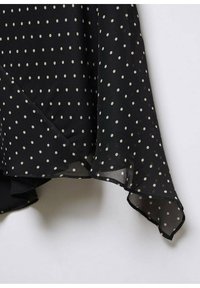 Tissu en chiffon noir à pois, avec un design fluide, comportant des pois blancs, un ourlet asymétrique et une légère transparence sur les bords.