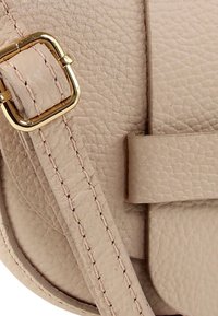 Beige leren handtas met een gestructureerd oppervlak, gouden beslag en een platte riem met zichtbare stiksels en een gespsdetail.