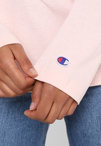 Lyserød langærmet skjorte med ribbede manchetter og lille broderet logo i blå og rød. Bæres med blå denimjeans.