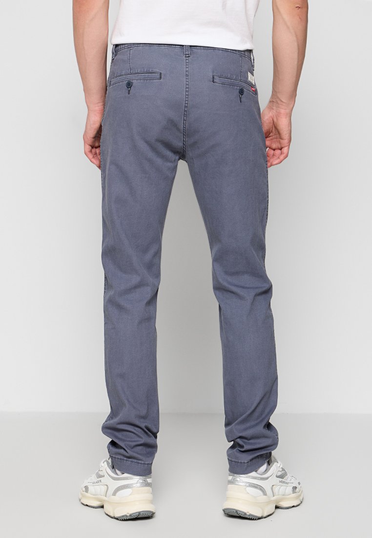 Pantalones de algodón grises con un corte ajustado, que cuentan con dos bolsillos traseros y una textura suave. Llevados con zapatillas blancas.