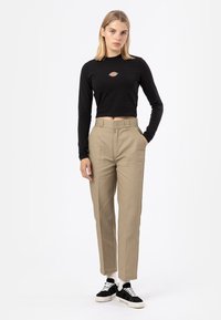Čierny dlhý rukáv crop top s vyšitým logom, v kombinácii s béžovými nohavicami s vysokým pásom a čiernymi teniskami s bielymi akcentmi.