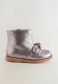 Metallic pink ankelstøvle med en knyttet detalje på siden, glat tekstur og en brun gummisål. Rund tå og kort skaft.