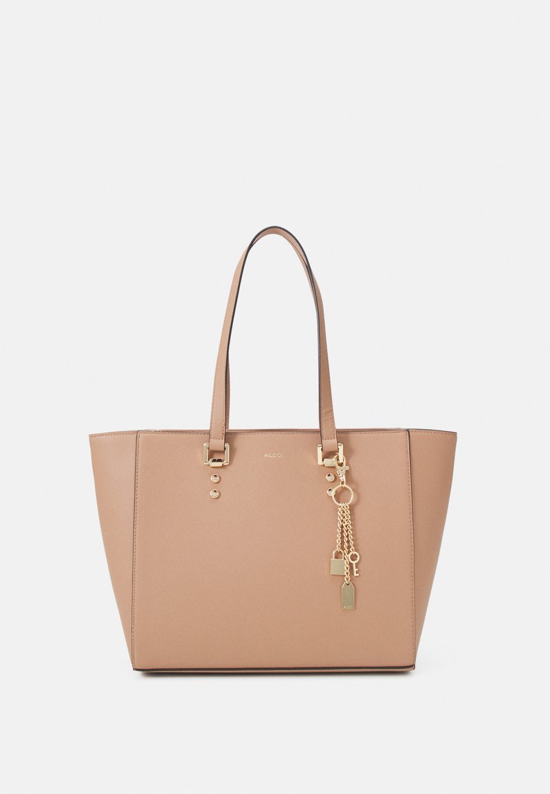 Beige tote bag with gold hardware, featuring a rectangular shape, dual top handles, and decorative charm with chains and tags.