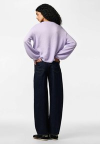 Violeta oversize džemperis no mīksta materiāla, kombinēts ar augsta vidukļa platajiem tumši zilā džinsa biksēm. Adīta tekstūra un brīvs piegriezums.