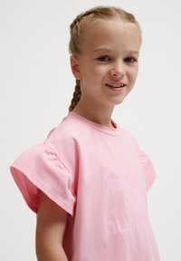 Ljusrosa bomulls t-shirt med rund halsringning och korta, puffärmar. Framsidan har en diskret, präglad logotyp.