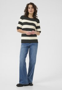 Haut à manches courtes à rayures gris foncé et crème, associé à un jean large bleu clair, des chaussures noires, en tissu texturé, coupe décontractée.