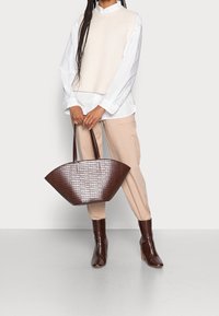 Sac en cuir synthétique marron effet crocodile, à ouverture large et dessus ouvert, avec deux longues poignées. La texture est brillante, avec une base plate et des côtés incurvés.