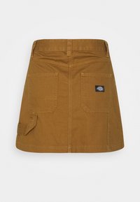 Mini-jupe en denim marron avec deux poches arrière, rabat de poche latérale et un petit patch logo Dickies noir sur la poche droite.