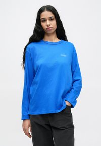 Μπλε βαμβακερό μπλουζάκι με μακριά μανίκια, στρογγυλή λαιμόκοψη και λογότυπο «OBEY». Η υφή φαίνεται απαλή· διαθ�έτει κάτω ραμμένους ώμους και άνετη εφαρμογή.