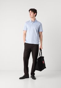 Polo de cor azul clara com mangas curtas, três botões e um pequeno logótipo no peito. Combinado com calças pretas e uma bolsa tote preta.